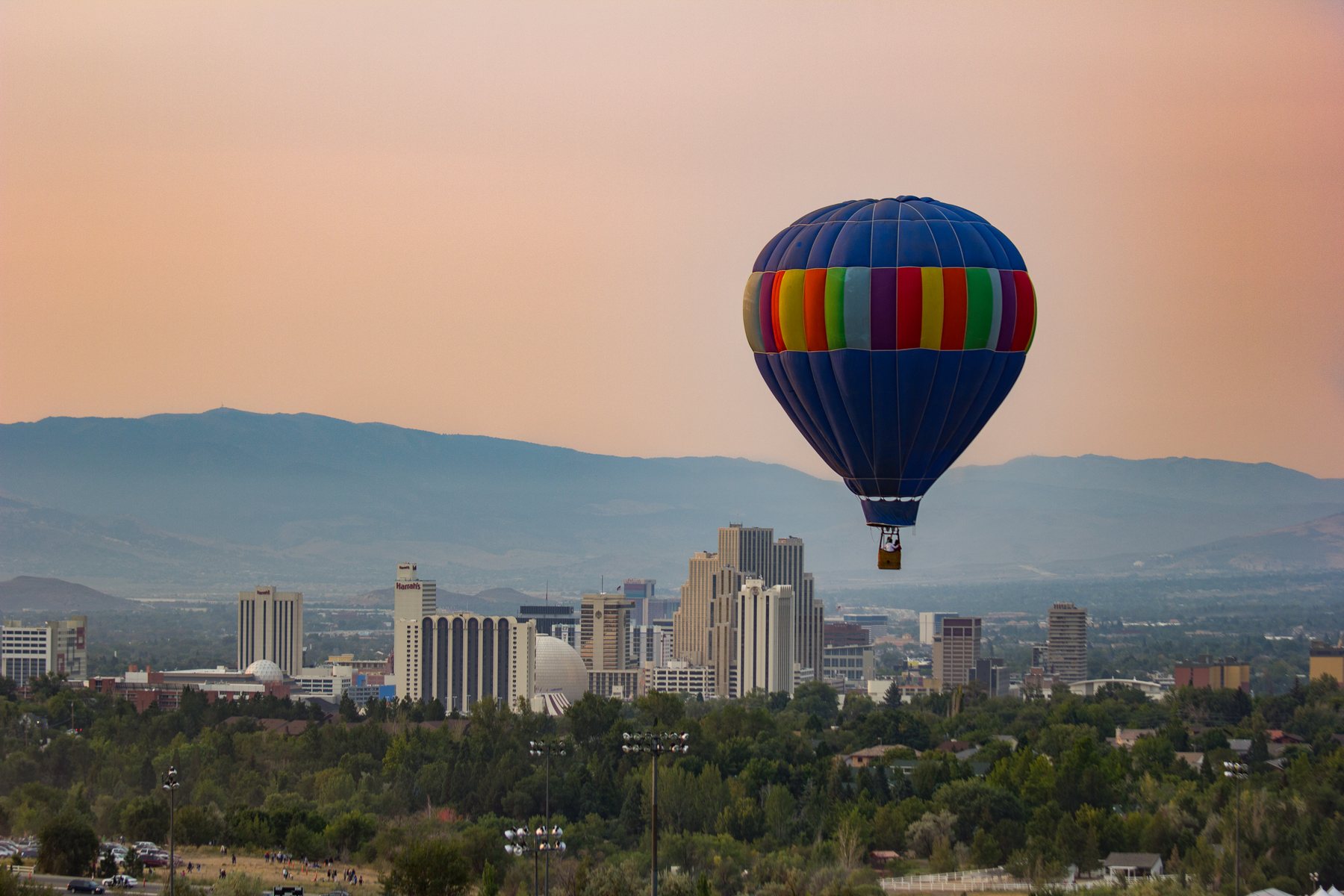 Multiple hot air balloons floating above Reno with the city skyline and Sierra Nevada mountains in the background.