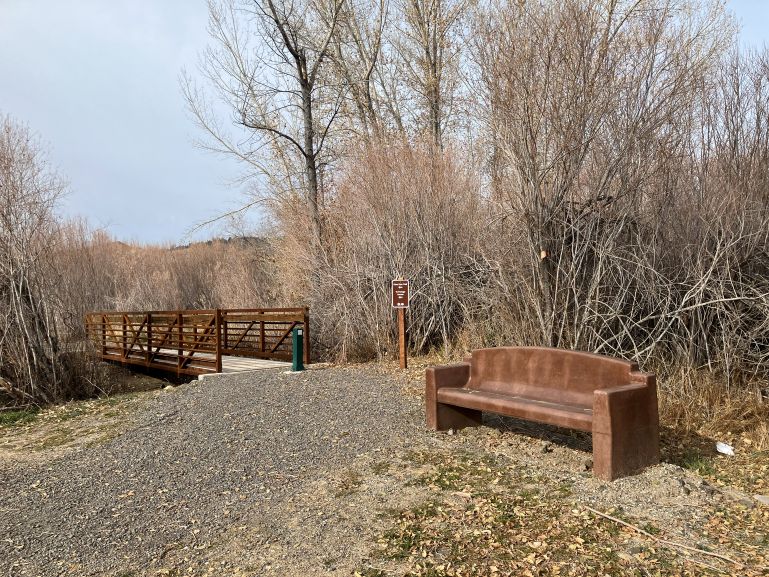 A cement bench conveniently located along a hiking path and bridge.